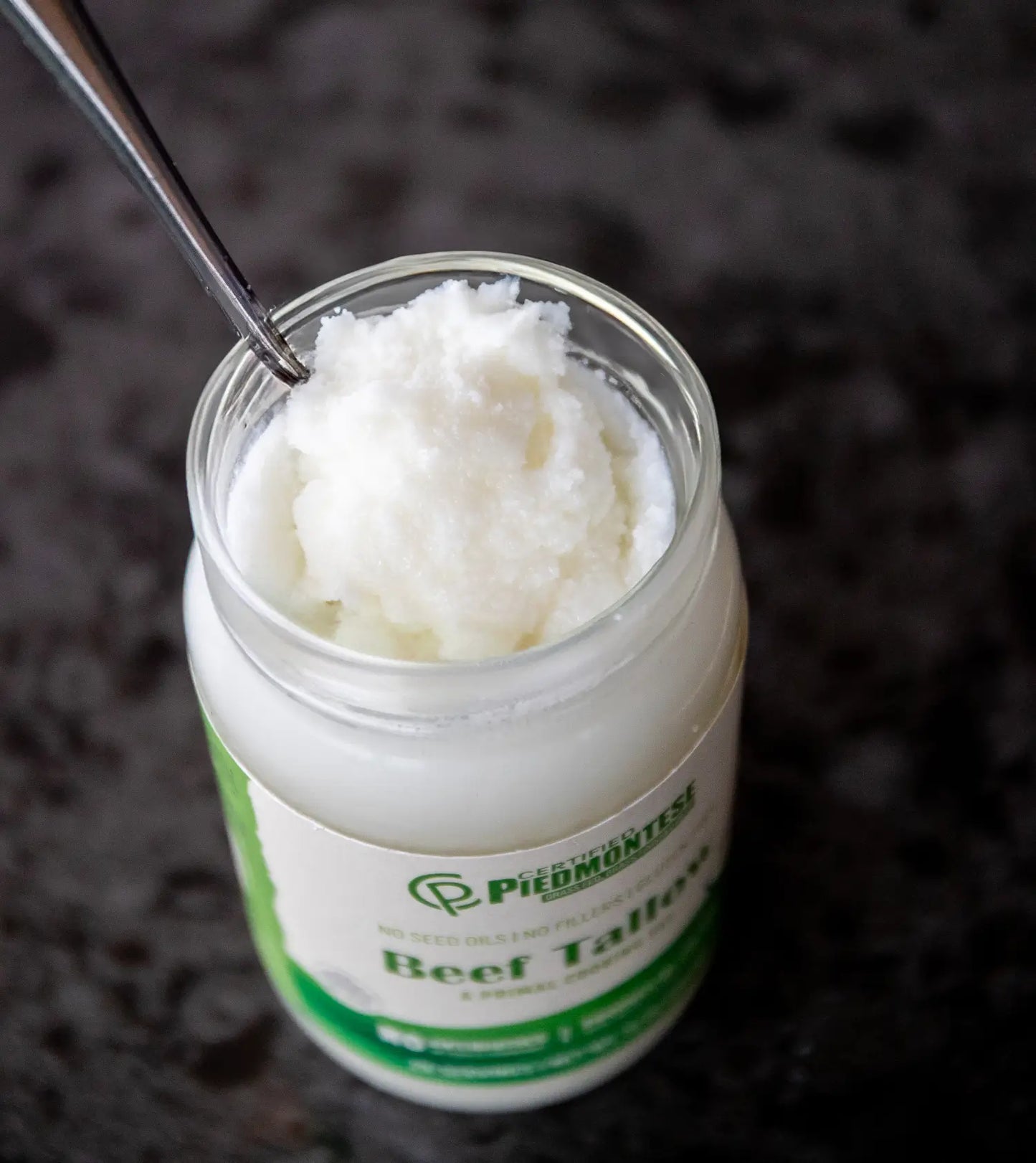 Jar of Piedmontese Beef Tallow with a spoon inside on a dark background