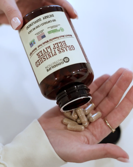 Hand holding a bottle of grass fed beef liver capsules with a white background