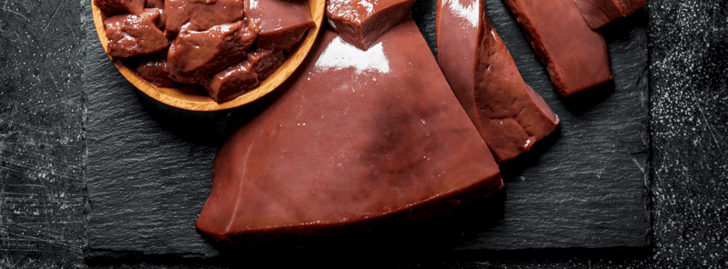 grass-fed beef liver sits on a black stone board with pieces of chopped liver in a yellow bowl
