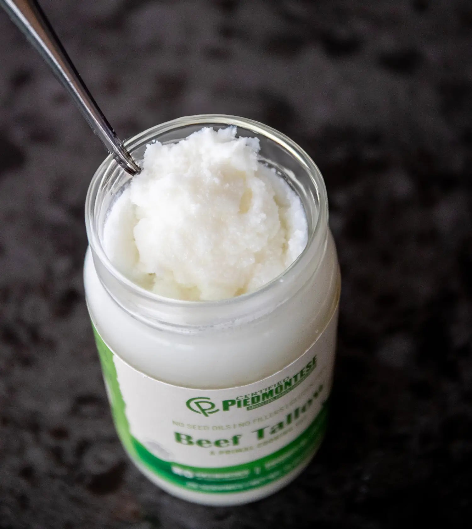 Jar of Piedmontese Beef Tallow with a spoon inside on a dark background
