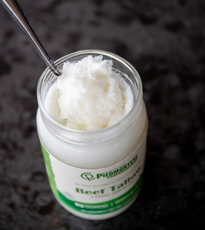 Jar of Piedmontese Beef Tallow with a spoon inside on a dark background